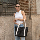 Woman carrying a black nylon tote bag with a cream strap over her shoulder.