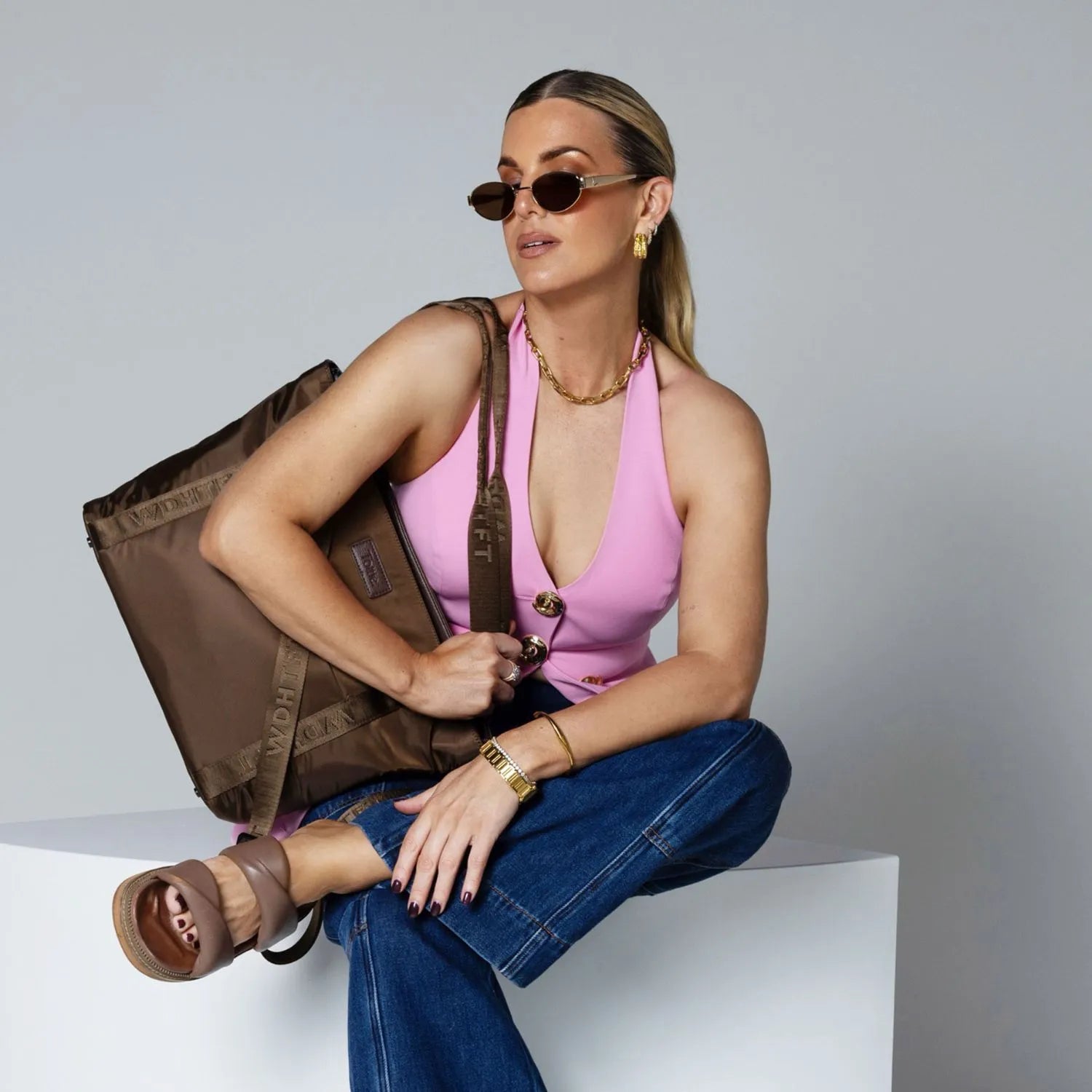 Woman sitting wearing shades and pink top with brown nylon tote bag on her shoulder.