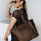 Stylish woman in brown top and sunglasses holding a brown nylon tote bag.