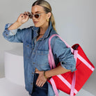 Woman wearing shades and denim jacket carrying a red nylon tote bag with pink strap.