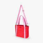 Angled side view of red nylon tote bag featuring pink strap embossed with WDHTFT logo against white background.