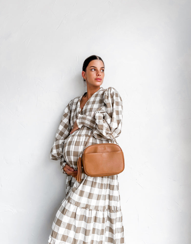 A pregnant woman wearing a dress carries a tan colour Crossbody Bag
