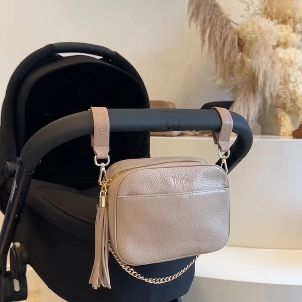 Stone colour vegan leather pram clips and matching crossbody bag attached to a pram stroller.