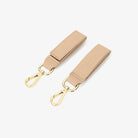 Pair of stone colour pram clips with gold hardware on white background – stylish and secure accessory for prams.
