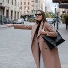 Woman dressed for work waving to catch a ride, black tote bag over her shoulder.