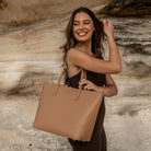 Side view of a woman carrying a tan tote bag on her shoulder.