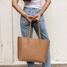 Back view of a woman carrying a tan tote bag.