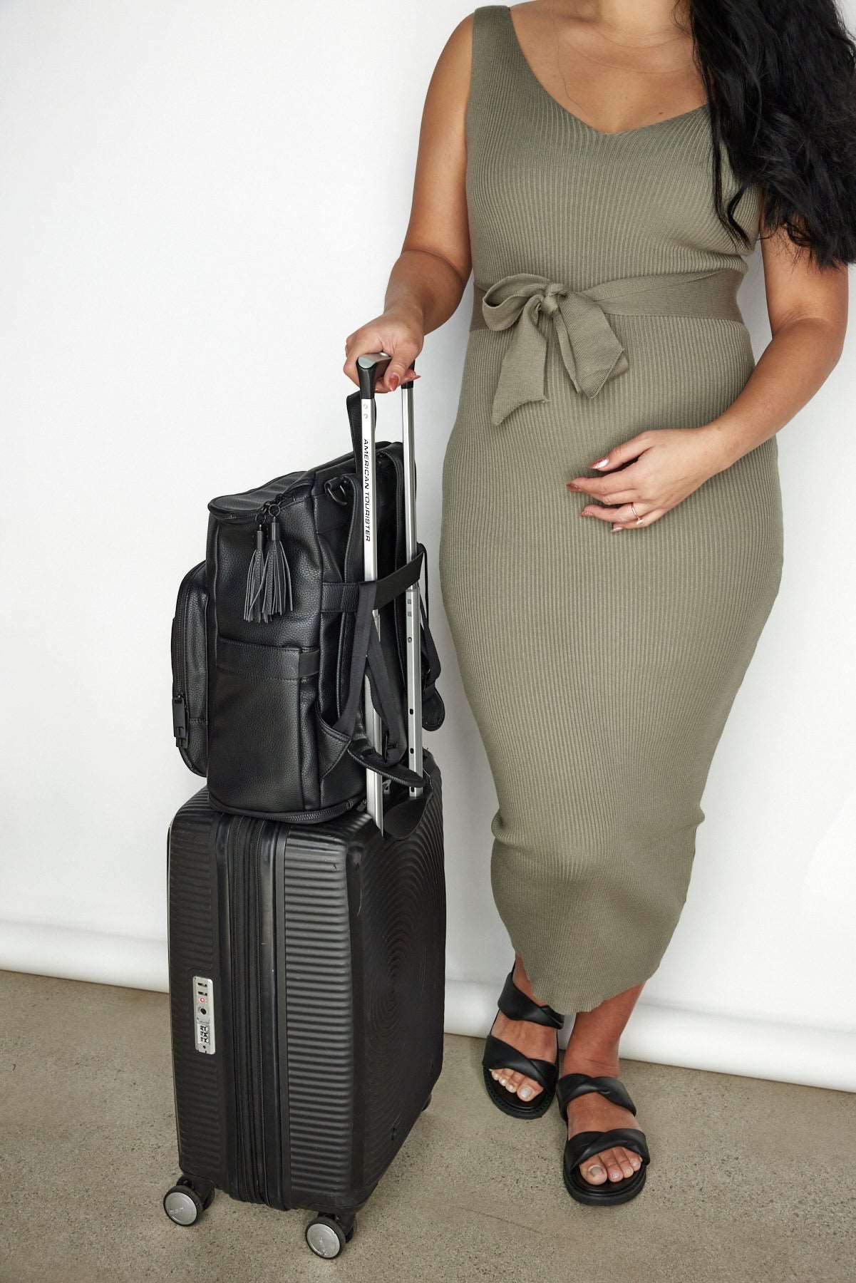 a pregnant woman holding  black luggage bag and a black travel backpack