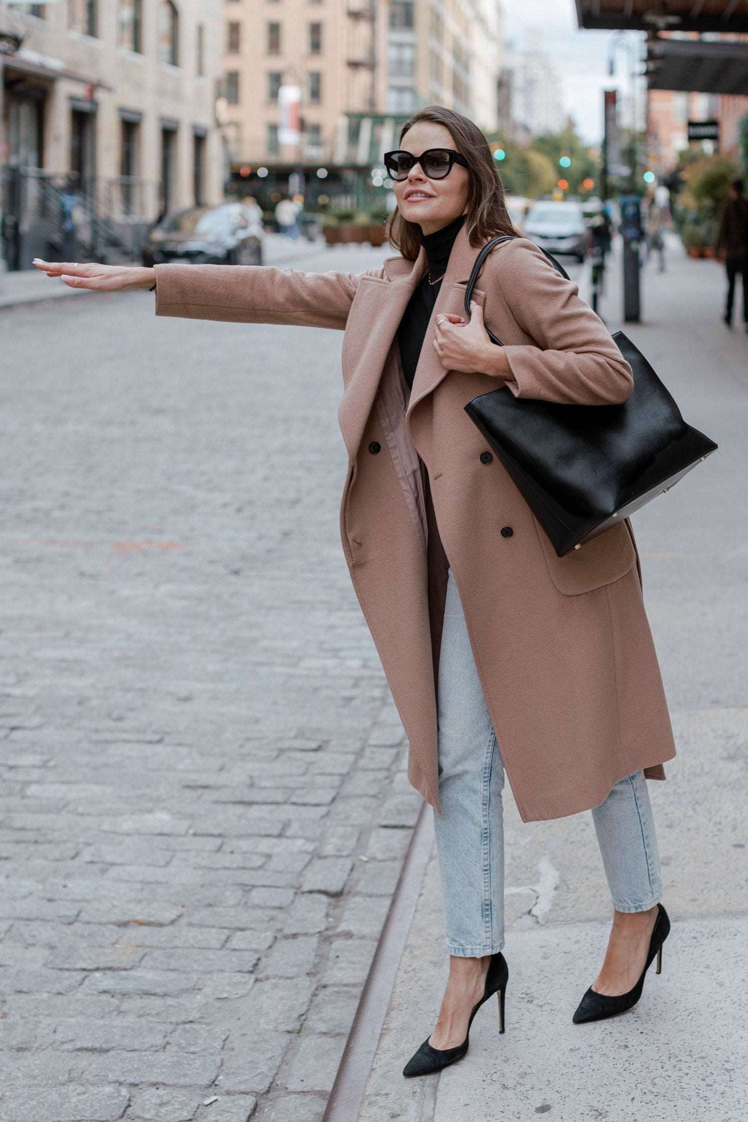 A woman in a coat and heels carrying a black tote bag