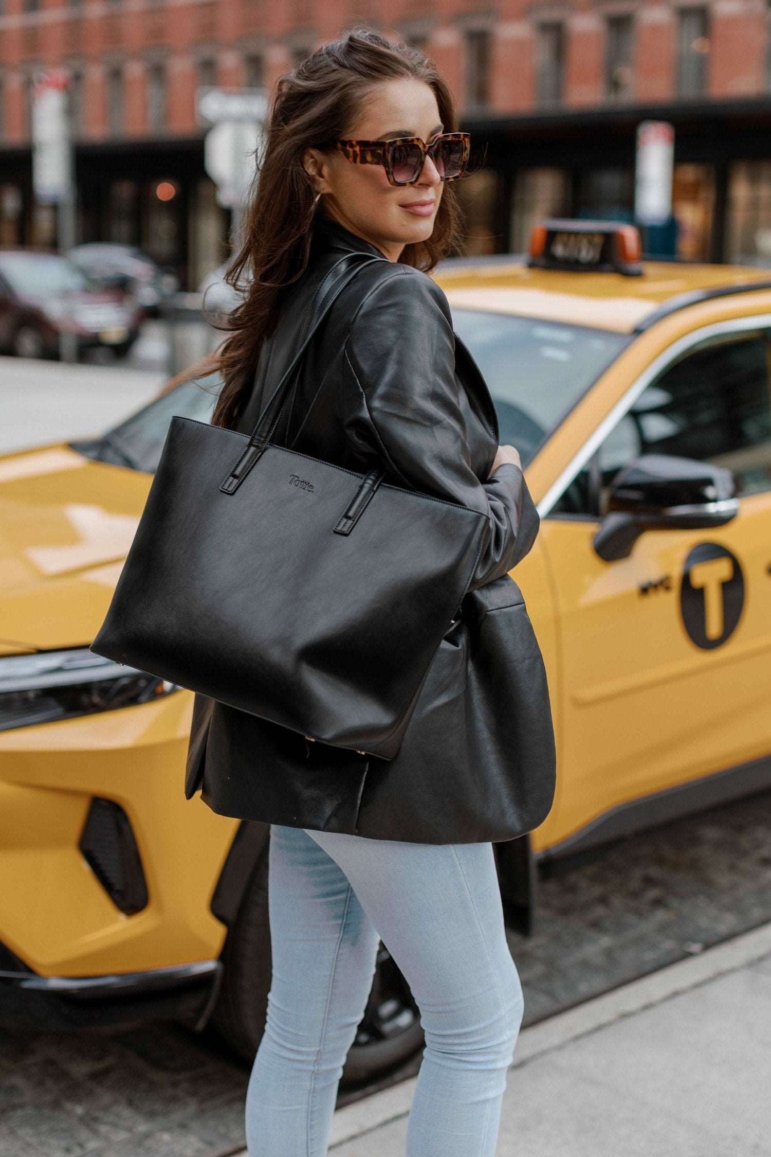 A woman dressed in jeans holds a black leather tote bag