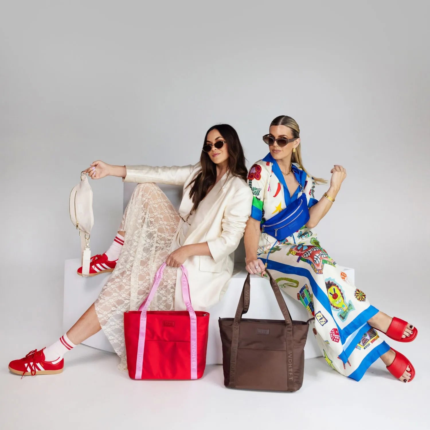 Woman wearing summer clothes with brown tote and blue bum bag, standing beside another woman in cream outfit carrying red nylon tote bag with pink strap, cream bum bag, and red shoes.