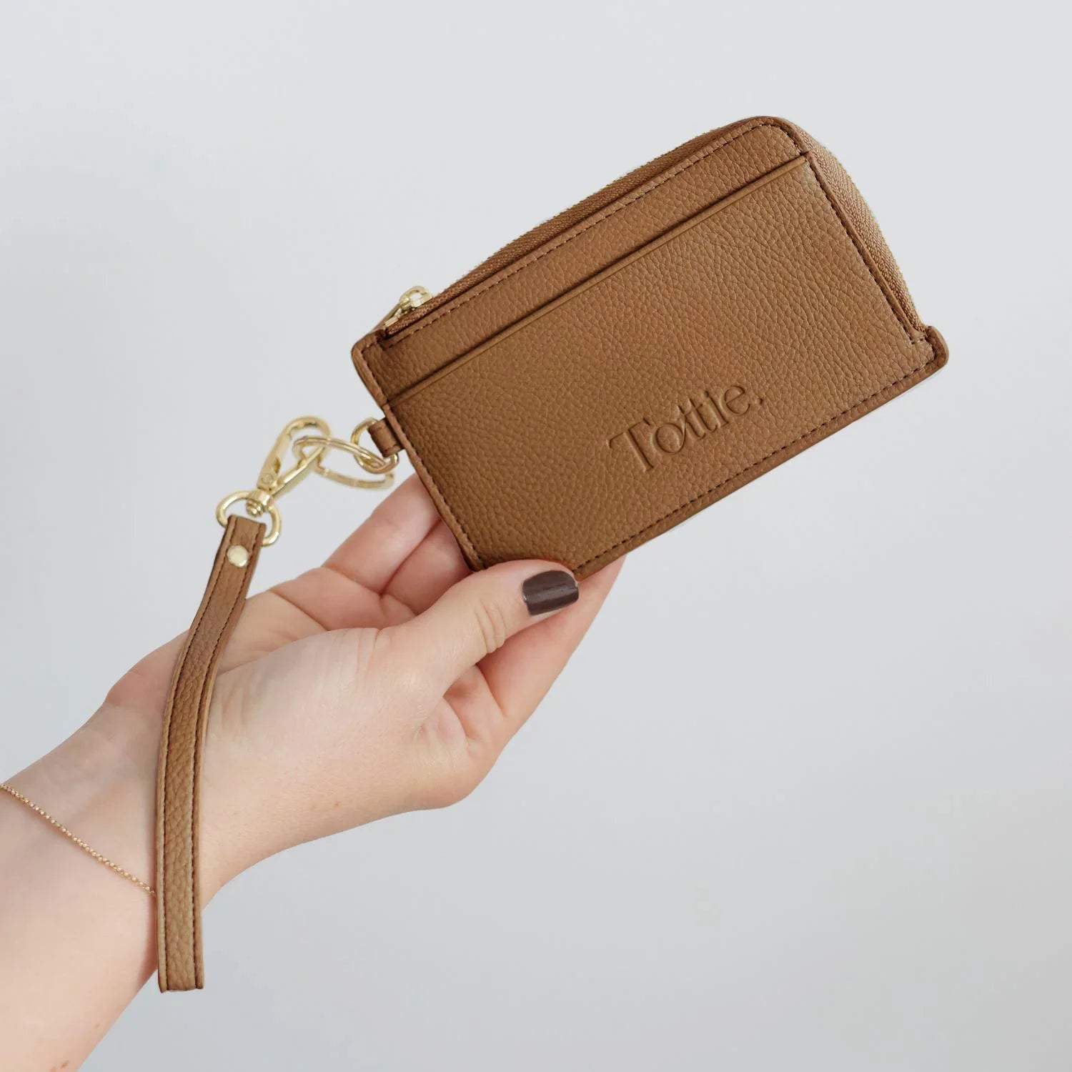 Hand holding a tan card holder wristlet wallet with gold hardware