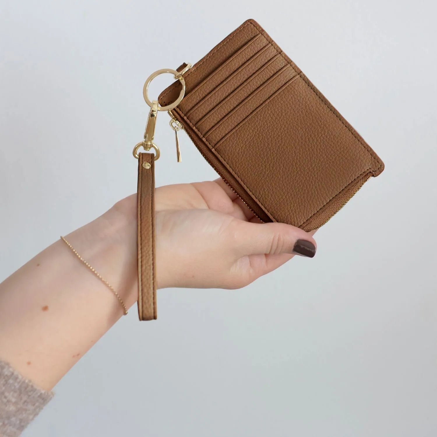 Tan leather card holder wristlet wallet with gold hardware held in hand.