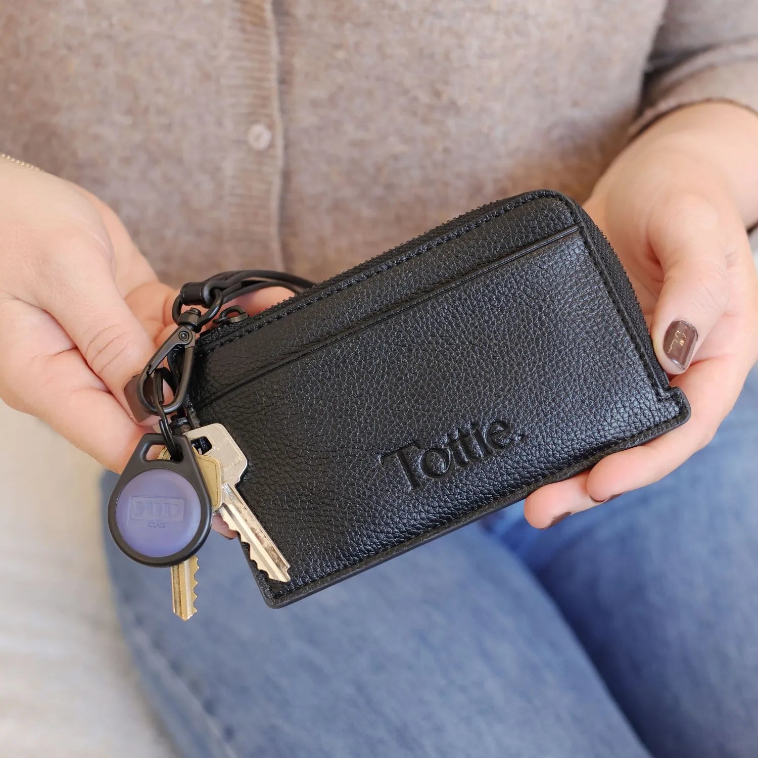 Close-up of black card holder wallet with key, held in hand, with jeans and brown top softly blurred in the background.