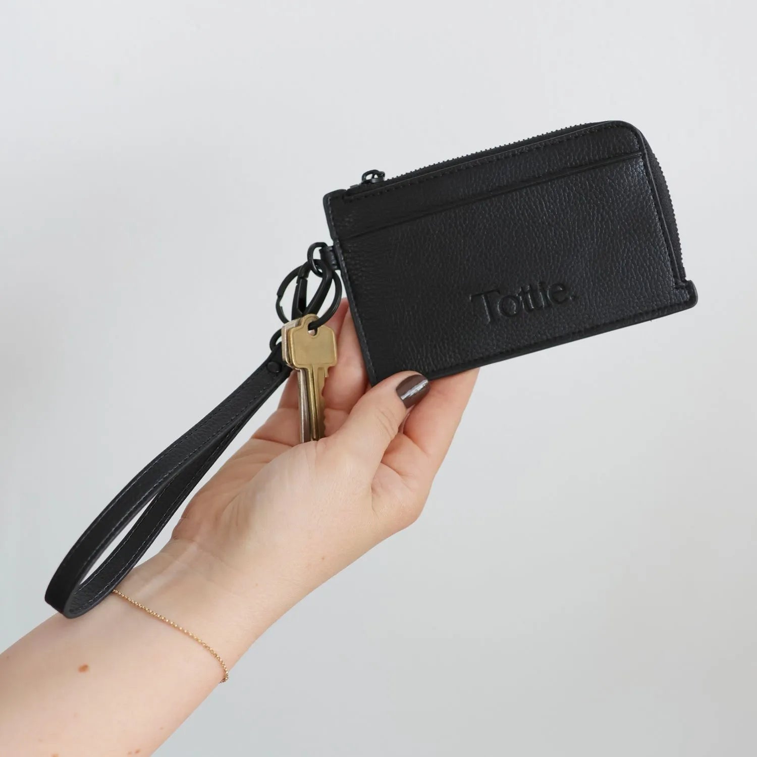 Black card holder wristlet wallet held by a hand.