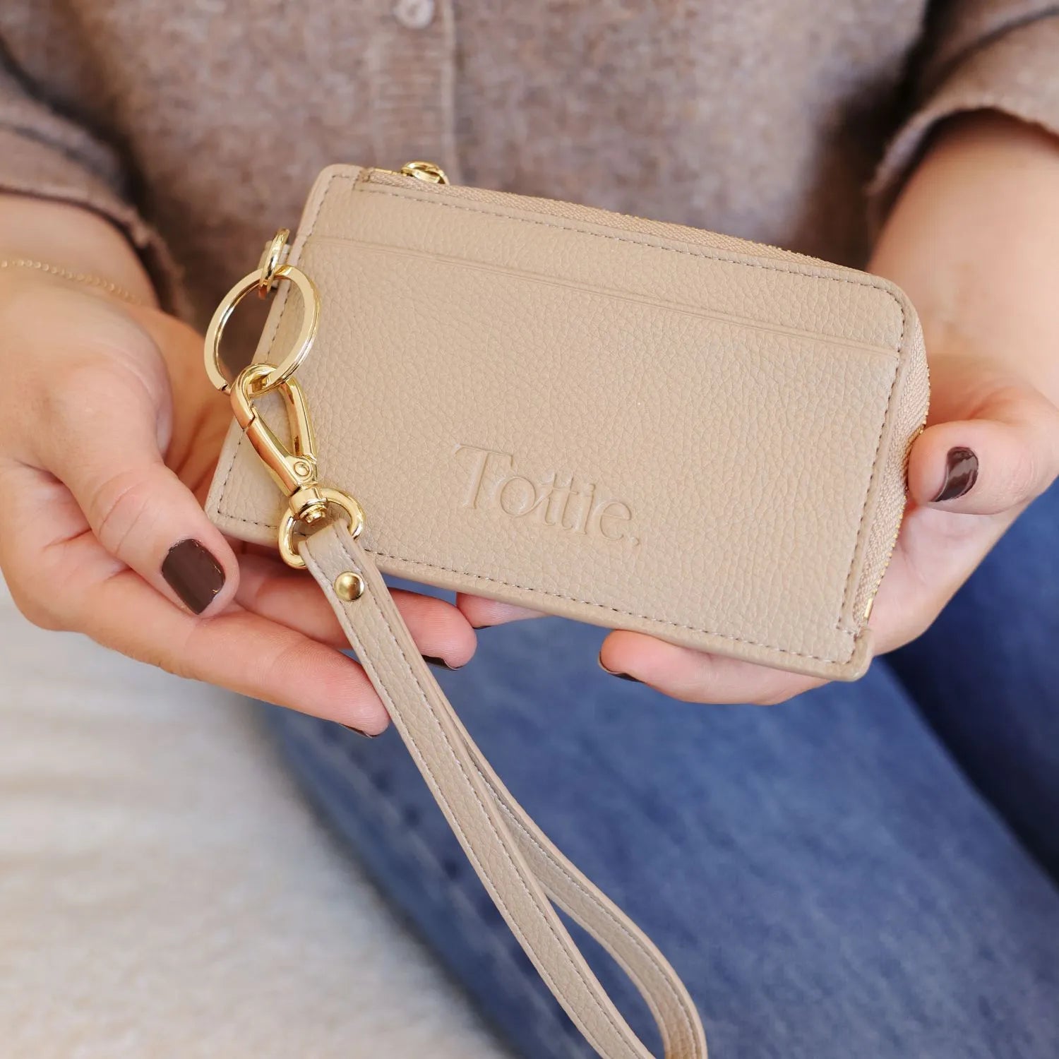 Stone card holder wallet with key, held in hand against a blurred backdrop of jeans and a brown top.