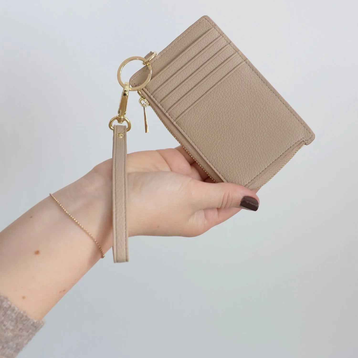 Close-up of a hand holding a stylish stone-coloured card holder wallet.