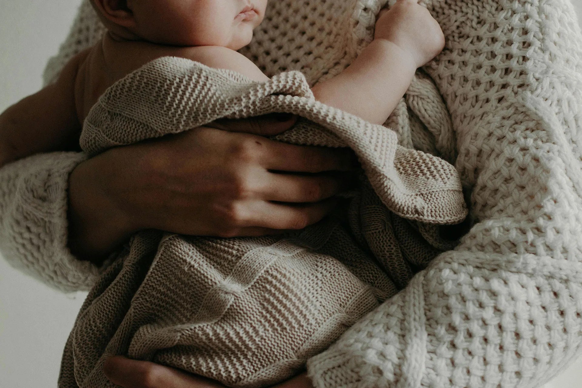 First-time mum holding her baby wrapped in a knitted swaddle – one of the best baby items 2025 for comfort and bonding