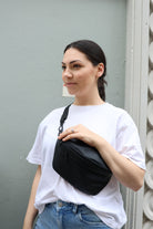 A woman dressed in a white shirt and jeans carries a black bum bag