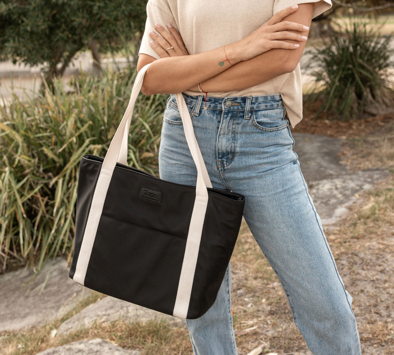 Woman holding a black tote bag in nylon with white straps outdoors for a casual look