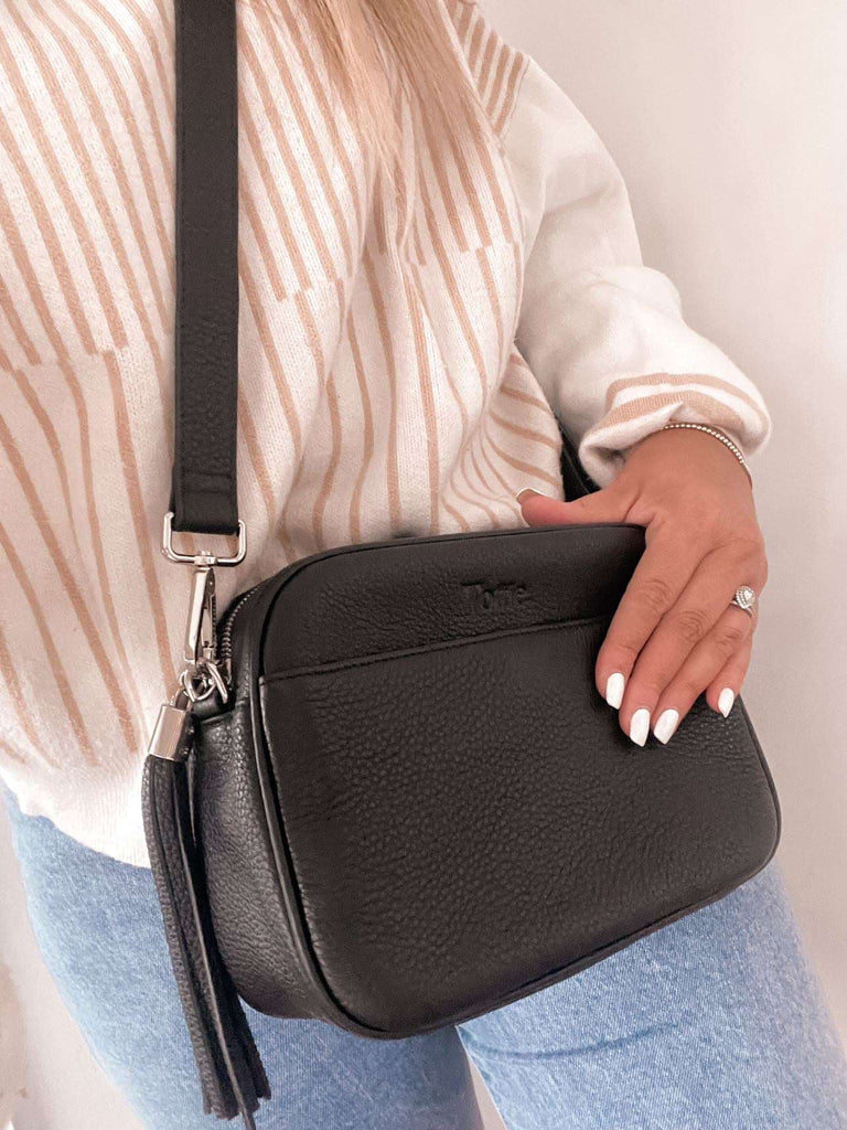 woman carrying a black leather crossbody bag with silver hardware
