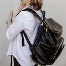 Person wearing a black nappy bag backpack with gold zippers against a plain background