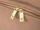 Close-up view of two gold zippers featuring the Tottie logo on a stone leather nappy backpack with a gold zipper from Tottie