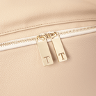 Close-up of a stone leather travel backpack with gold zipper pulls featuring initials.