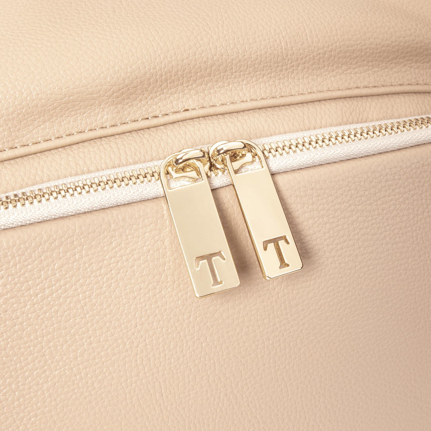 Close-up of a stone leather travel backpack with gold zipper pulls featuring initials.