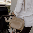 Woman pushing a pram, while holding a beige crossbody bag with a chain detail 