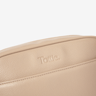 Beige leather crossbody bag with 'Tottie' logo on a light beige background