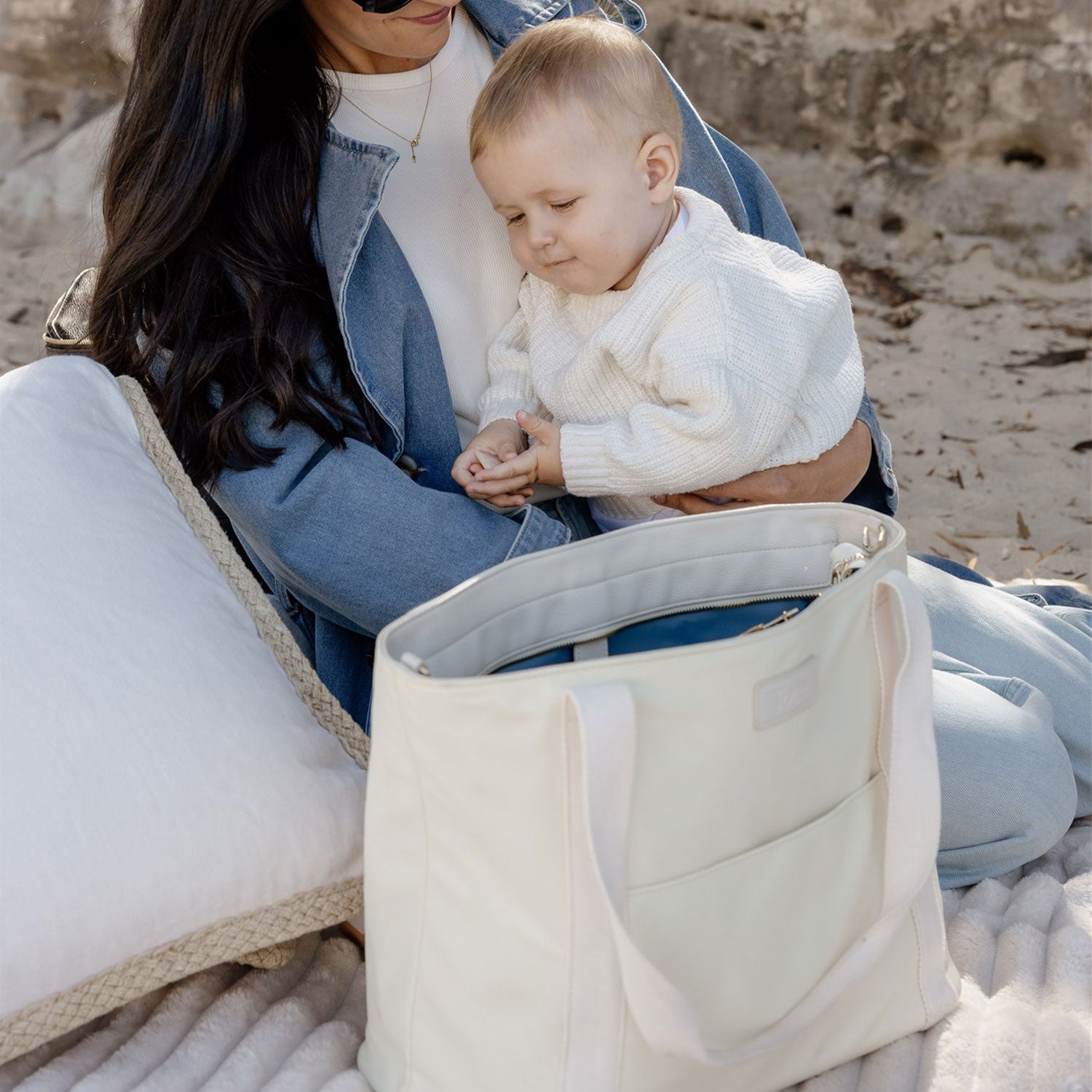 Woman holding a baby on a beach with a beige nappy tote bag in front