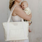 Mother holding a baby and a pastel tote bag against a plain background