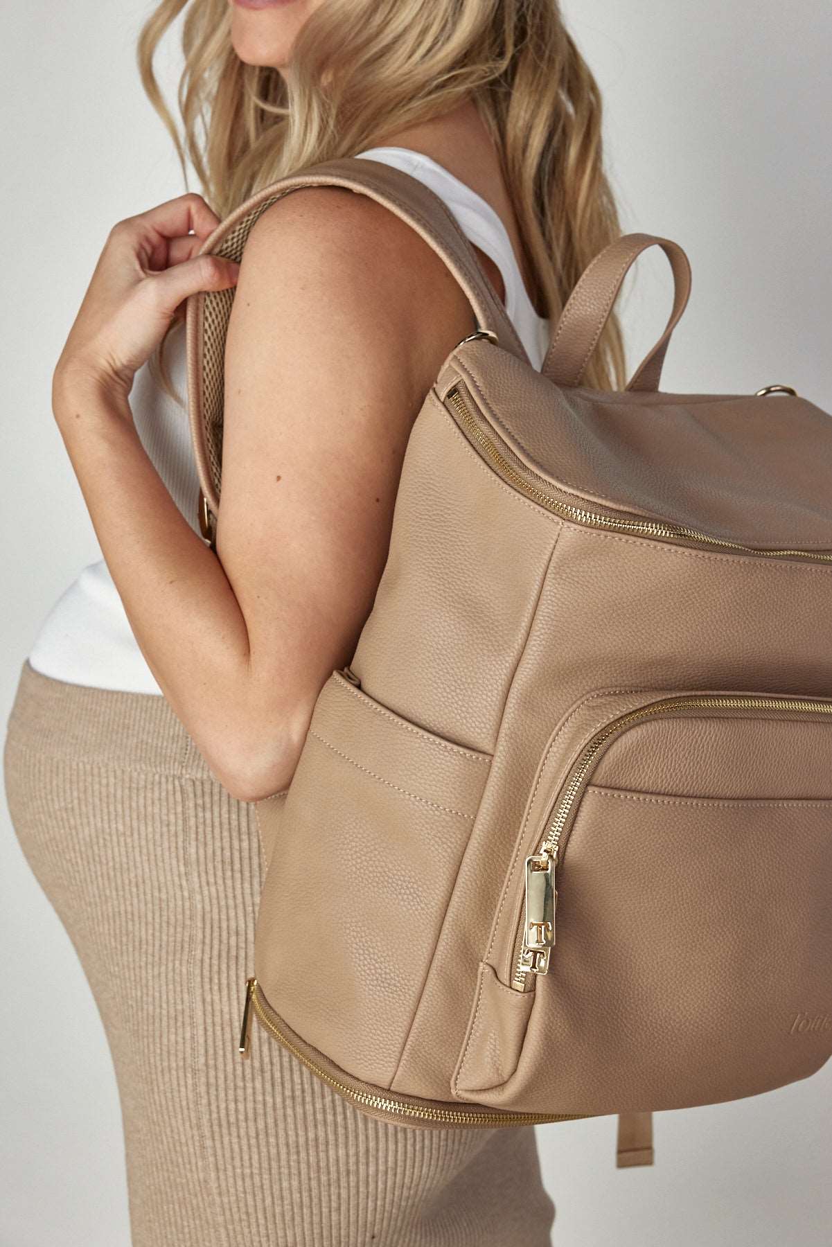 Pregnant woman carrying a stone leather nappy backpack with a gold zipper from Tottie