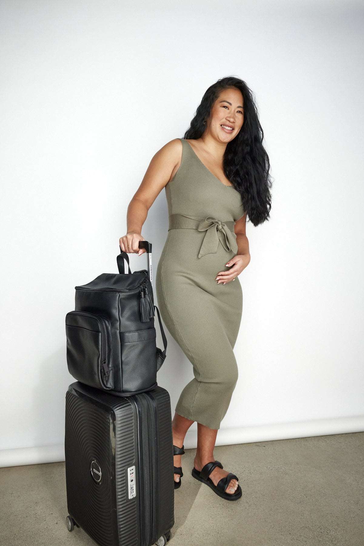 a pregnant woman holding  black luggage bag and a black travel backpack