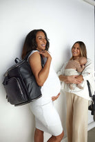 Two women with a baby, one of them carrying a black travel backpack