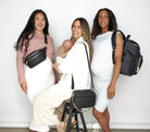 Three women smile while posing with a baby and each one carrying a bum bag