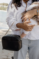 Person holding a black handbag with a chain strap on a beach.