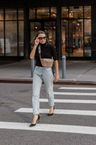 A woman in jeans and a black top crosses the street carrying a bum bag