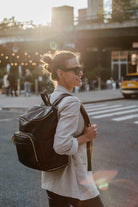 A woman in sunglasses carries a black leather travel backpack