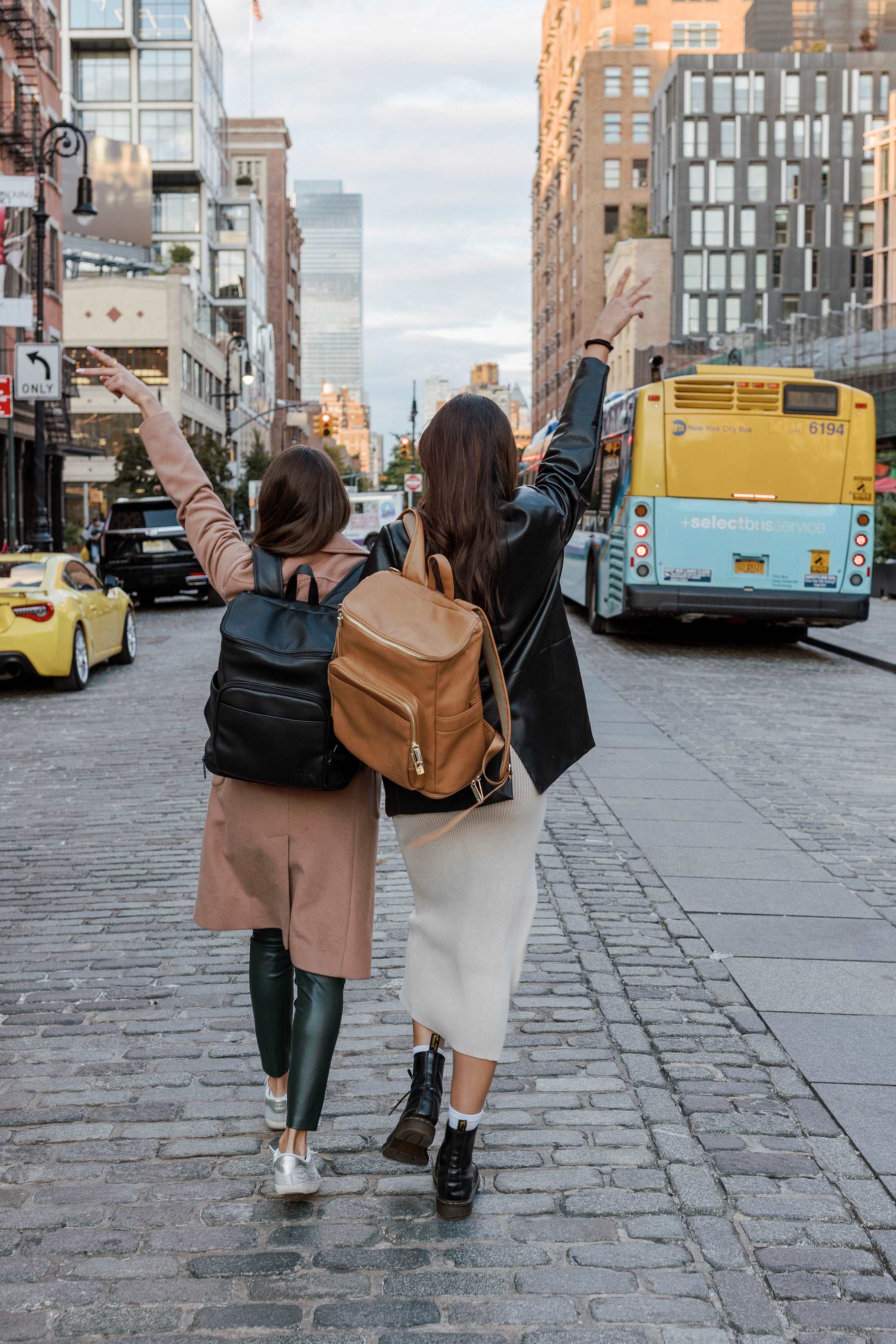 Two women walks down a street, each carrying a travel backpack