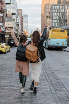 Two women walks down a street, each carrying a travel backpack