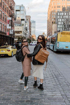 Two women walks down a street, each carrying a travel backpack
