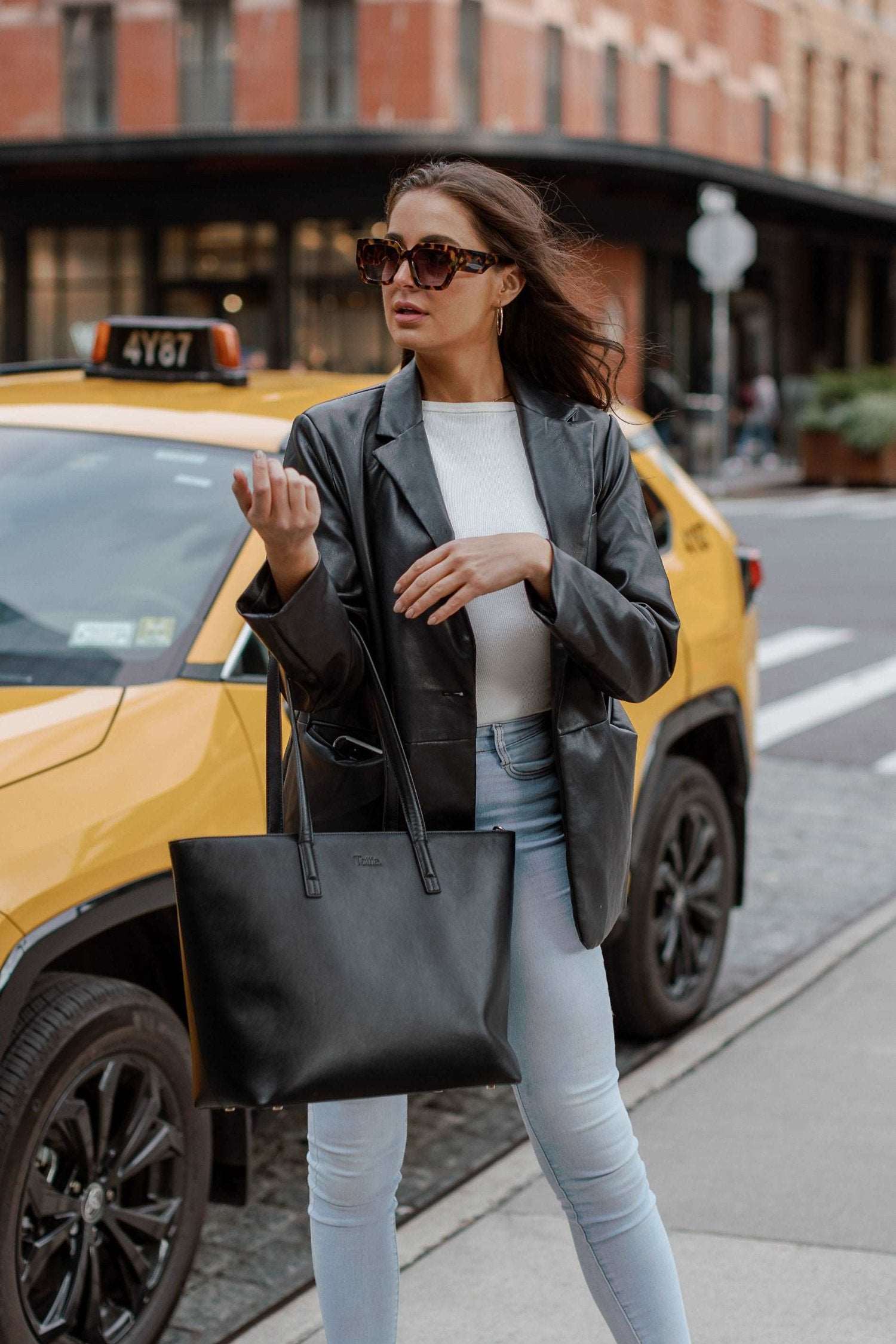 A woman dressed in jeans holds a black leather tote bag
