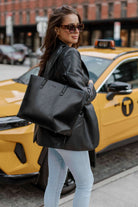 A woman dressed in jeans holds a black leather tote bag