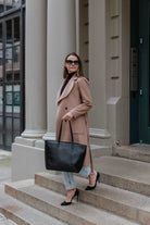 A woman in a coat and heels carrying a black tote bag
